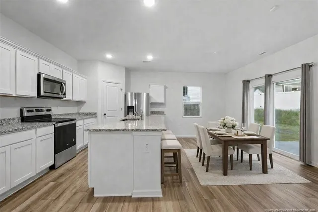 a kitchen with granite countertop a stove top oven a sink dishwasher a refrigerator and white cabinets with wooden floor