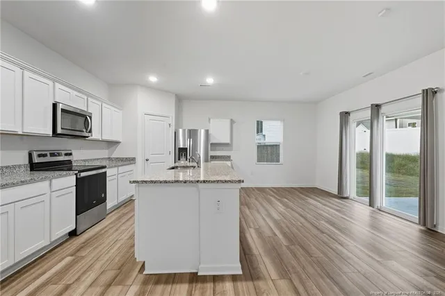 a kitchen with granite countertop a stove top oven a sink dishwasher a refrigerator and white cabinets with wooden floor