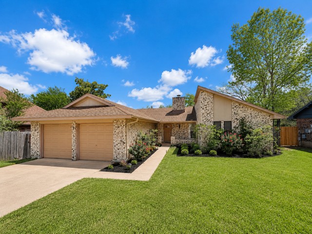 A striking stone facade with a manicured lawn awaits, featuring an attached garage and inviting landscaping.