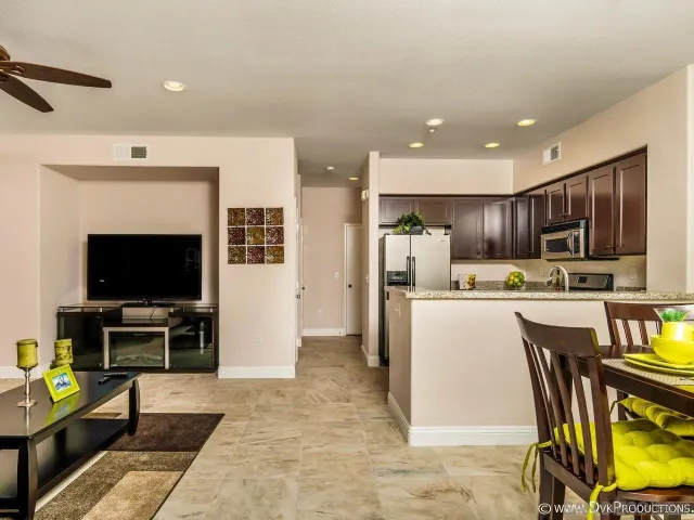 a living room with stainless steel appliances furniture a flat screen tv and kitchen view