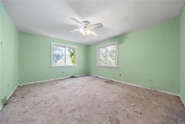 an empty room with chandelier fan and windows