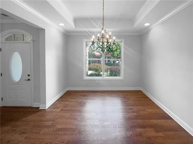 an empty room with wooden floor chandelier and windows