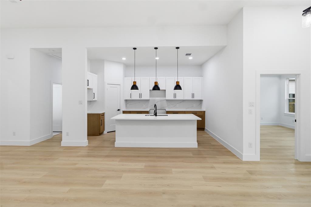 1119 Riverwood Road Dallas, TX 75217 - Photo 32 of 32 Kitchen with decorative light fixtures, an island with sink, white cabinetry, light wood-style floors, and open floor plan