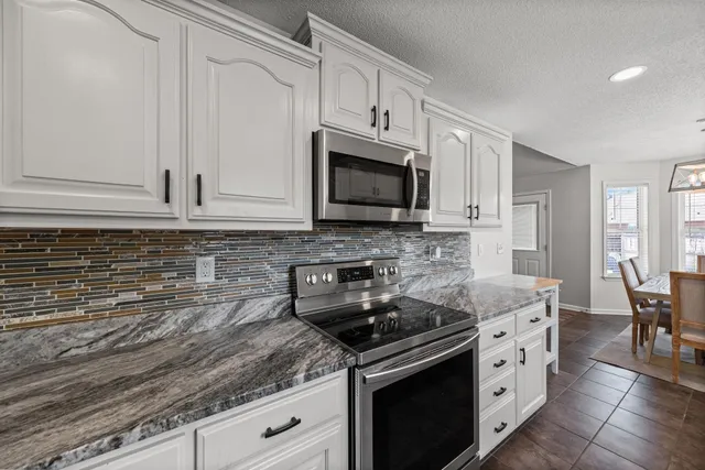 a kitchen with granite countertop white cabinets stainless steel appliances and a counter space