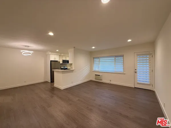 an empty room with wooden floor kitchen view and a window