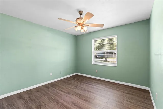 an empty room with wooden floor chandelier fan and windows