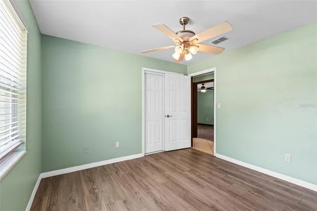 an empty room with wooden floor chandelier fan and windows