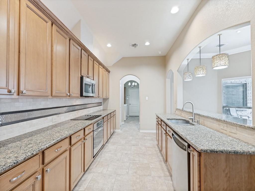 10032 Bell Rock Road Frisco, TX 75035 - Photo 14 of 23 Galley kitchen featuring extensive wood-finish cabinetry, granite countertops, and a tile backsplash with decorative accents. Glass panty door at far end.
