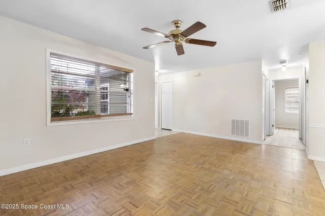 an empty room with chandelier fan and windows