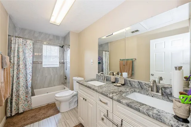 a bathroom with a granite countertop double vanity sink toilet mirror and shower
