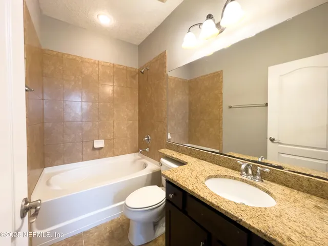 a bathroom with a granite countertop bathtub sink vanity mirror and toilet