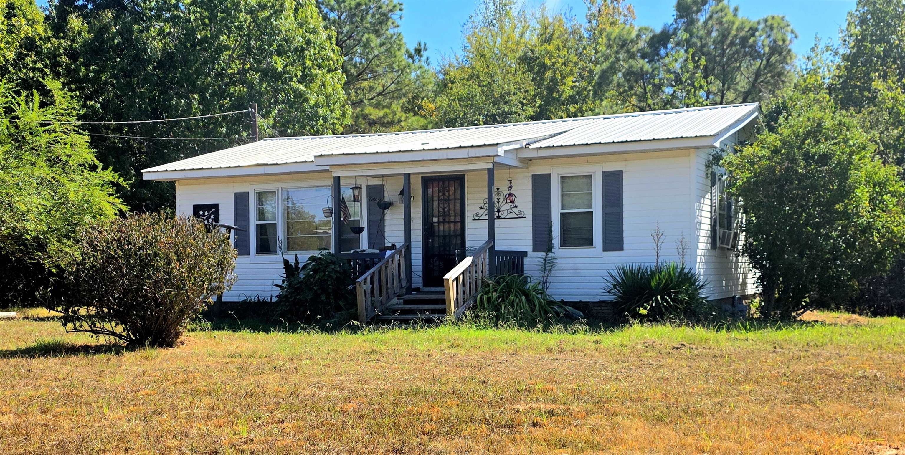 2871 Purdy Road Selmer, TN 38375 - Photo 1 of 1 White siding exterior with a metal roof, front porch, and mature surrounding trees
