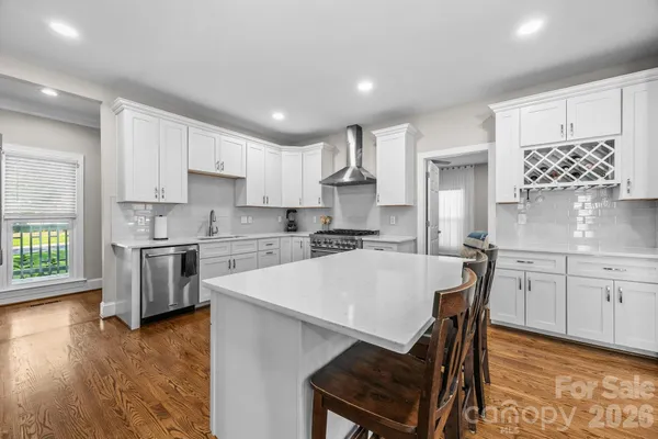 a white kitchen with a stove a sink a microwave a center island and cabinets