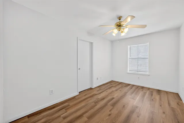a view of an empty room with chandelier fan and wooden floor