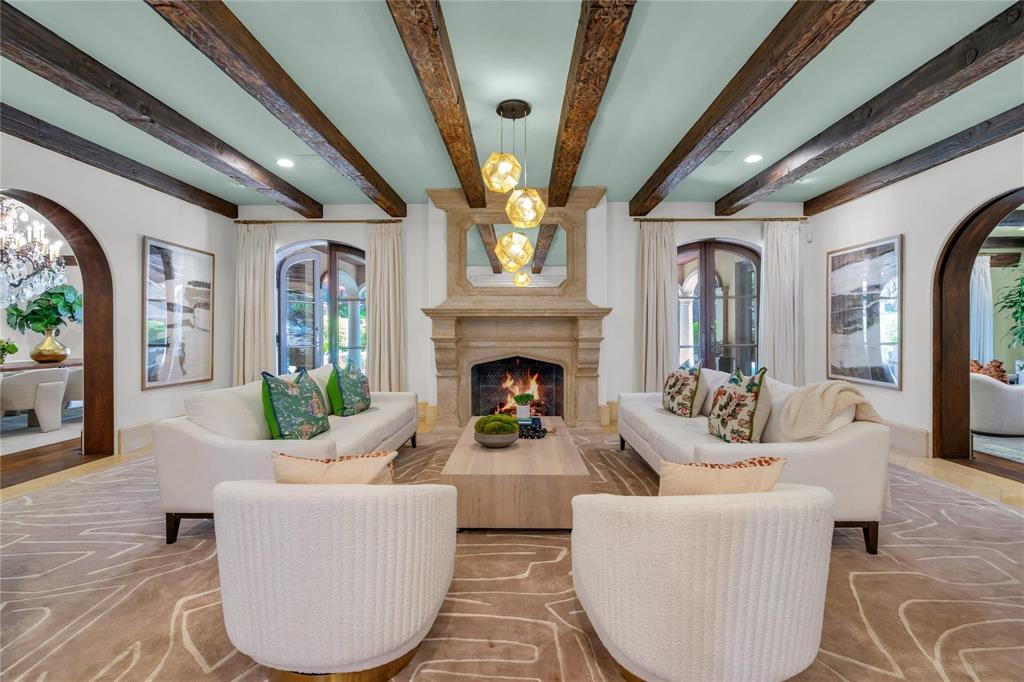 4612 Watauga Road Dallas, TX 75209 - Photo 13 of 32 Living space featuring a stone fireplace with a lit fire, exposed wood beams on the ceiling, and arched doorways