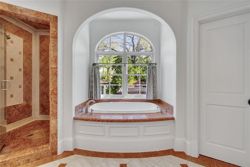 4612 Watauga Road Dallas, TX 75209 - Photo 22 of 32 Bathroom featuring a built-in bathtub with a natural stone surround, an arched window, and a glass-enclosed shower with natural stone tiling