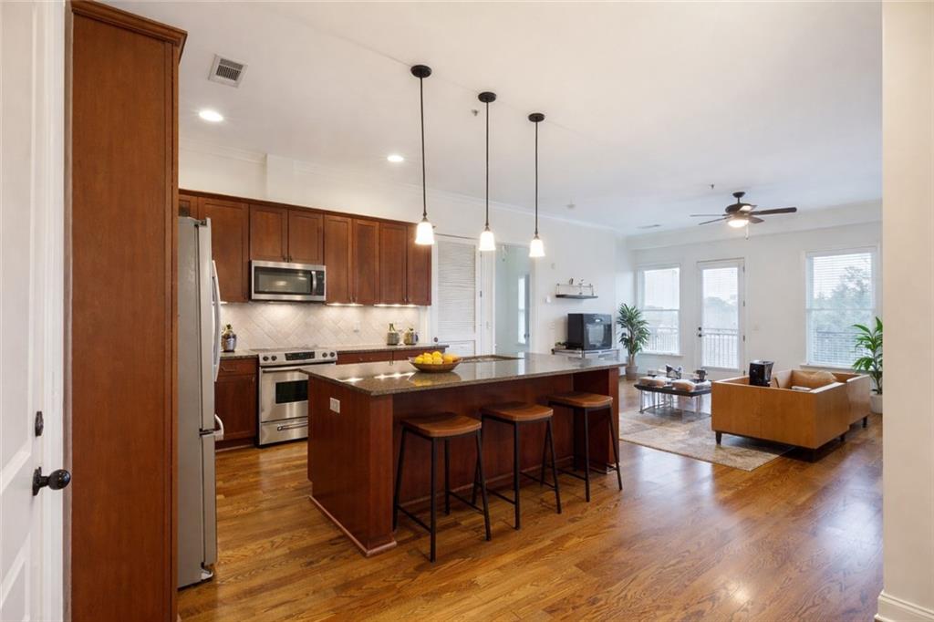 a kitchen with stainless steel appliances granite countertop wooden floors stove top oven and couches