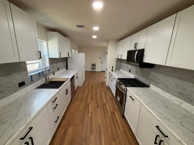 a large kitchen with a stove top oven a sink a microwave and wooden floor