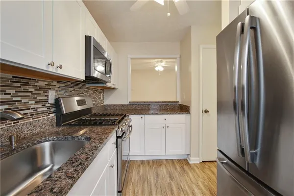 a view of a refrigerator in kitchen and an empty room with wooden floor