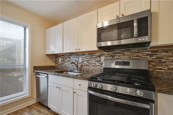 a kitchen with granite countertop a sink stainless steel appliances and white cabinets