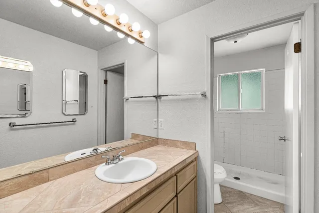 a bathroom with a granite countertop sink a toilet a mirror and shower