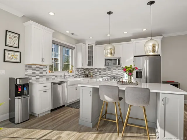 a kitchen with stainless steel appliances kitchen island granite countertop a dining table chairs and white cabinets