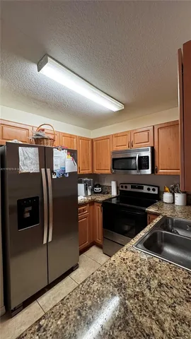 a kitchen with stainless steel appliances granite countertop a refrigerator a stove and a sink with wooden floors