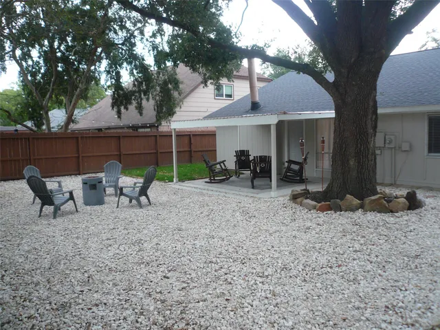 a view of a patio with table and chairs under an umbrella with large trees