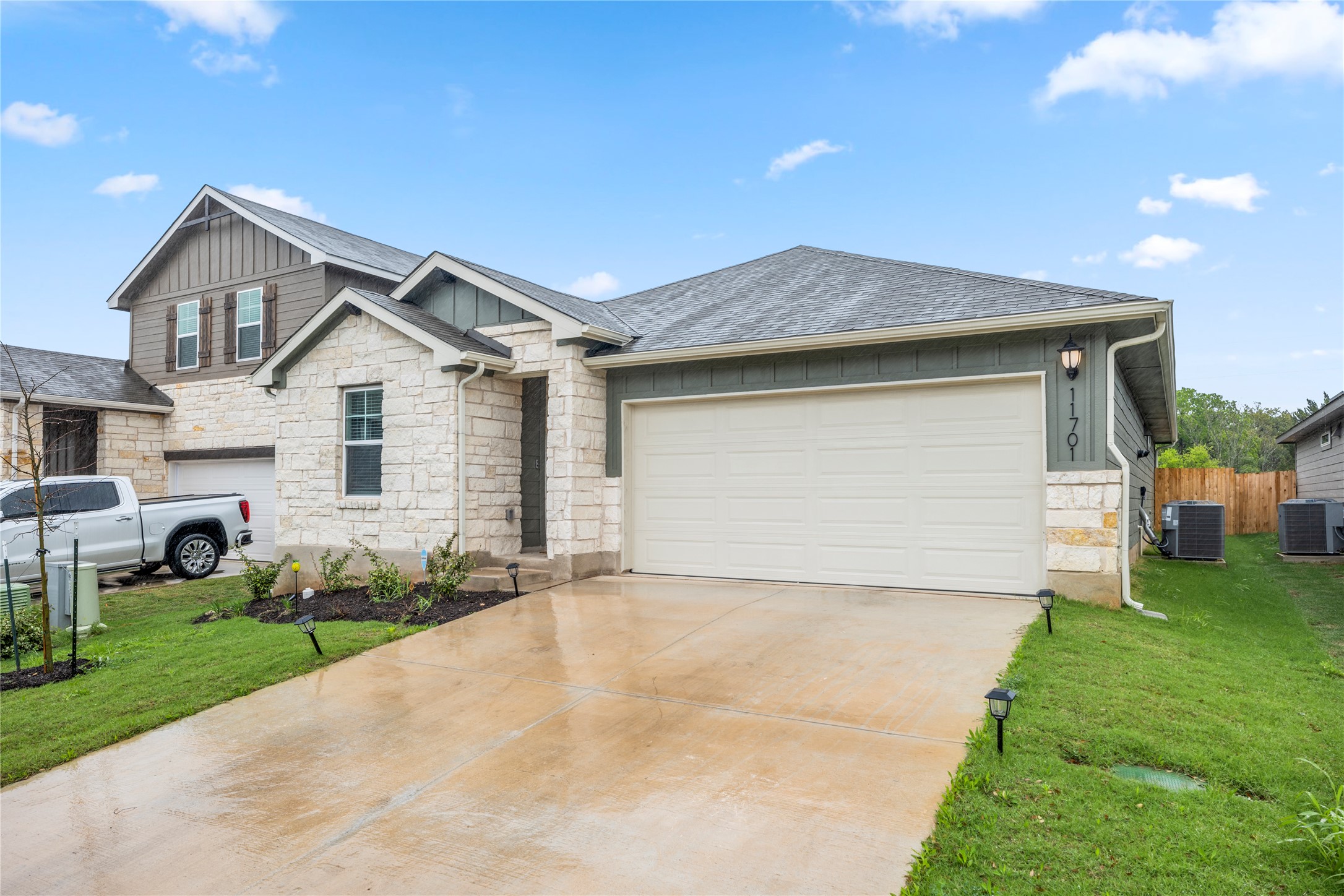 View of front of home featuring board and batten siding, concrete driveway, stone siding, a front lawn, and an attached garage