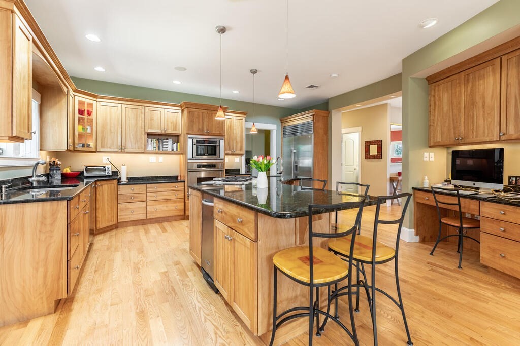 101 Clarke Circle Needham, MA 02492 - Photo 7 of 31 a kitchen with stainless steel appliances kitchen island granite countertop a stove top oven a sink a dining table and chairs with wooden floor