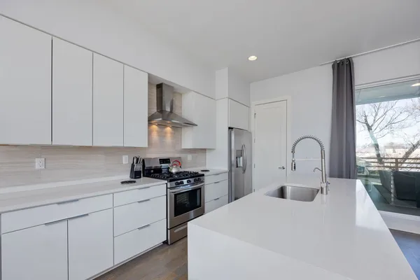 a kitchen with stainless steel appliances granite countertop a sink a stove a refrigerator and white cabinets with wooden floor
