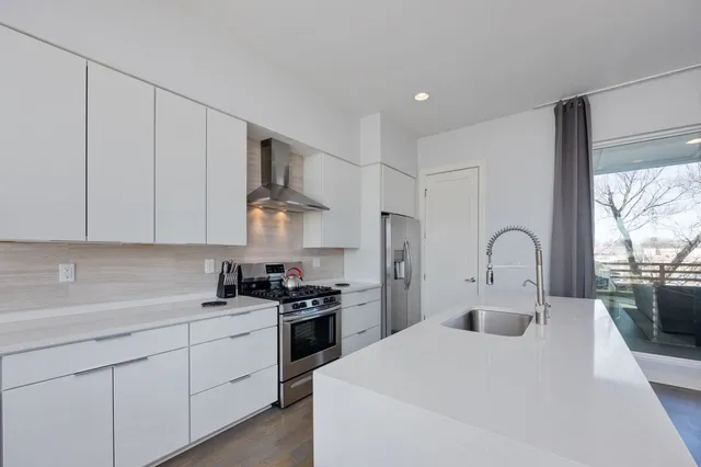 a kitchen with stainless steel appliances granite countertop a sink a stove a refrigerator and white cabinets with wooden floor