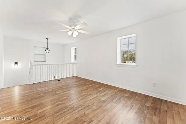 an empty room with wooden floor ceiling fan and windows