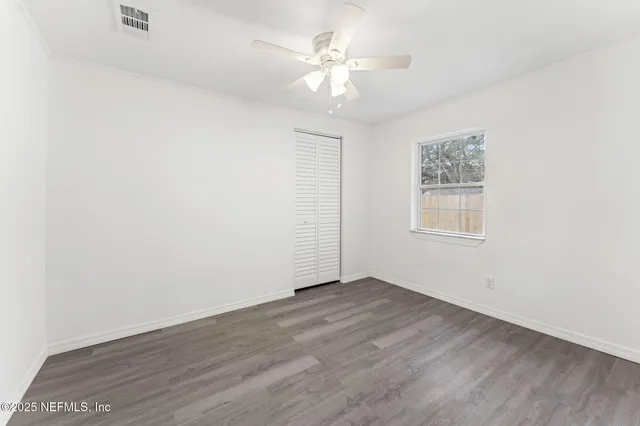 an empty room with wooden floor chandelier fan and windows