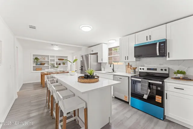 a white kitchen with a stove top oven a sink dishwasher and white cabinets with wooden floor