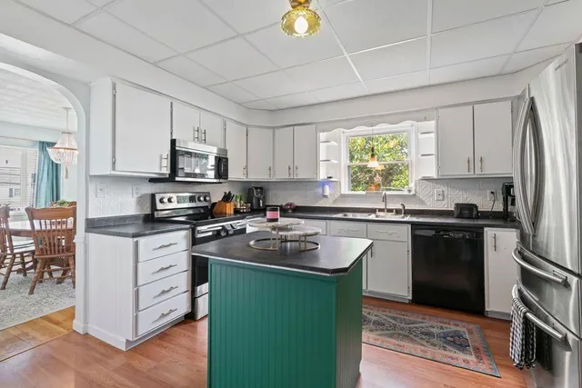 a kitchen with kitchen island granite countertop white cabinets appliances and a window