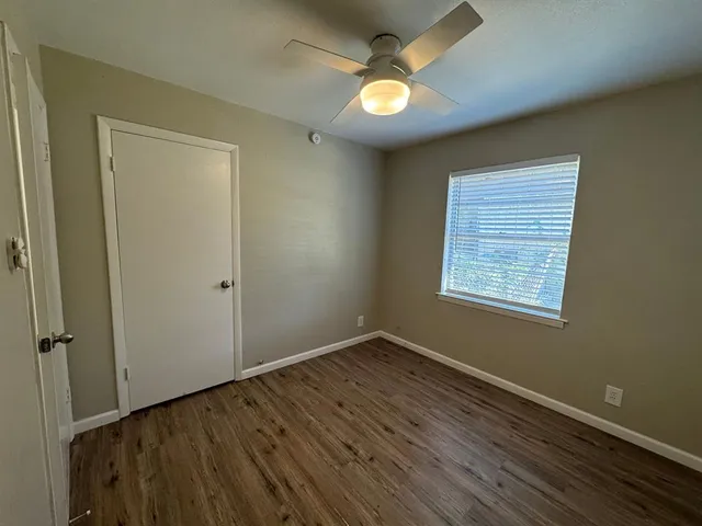 an empty room with wooden floor fan and windows