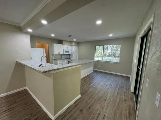 a kitchen with stainless steel appliances granite countertop a refrigerator a sink dishwasher a stove and white countertops with wooden floor