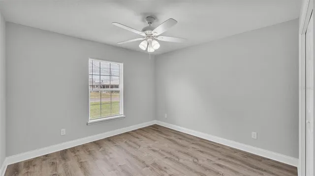 an empty room with wooden floor fan and windows