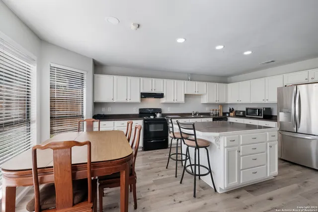 a kitchen with stainless steel appliances granite countertop a dining table chairs refrigerator and microwave