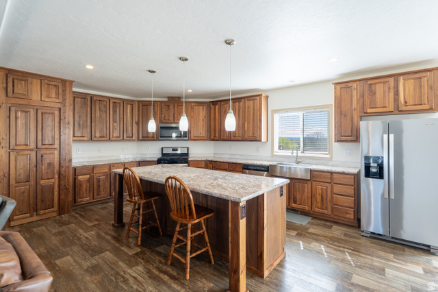 700 East Peter Springs Road Monticello, UT 84535 - Photo 8 of 57 Spacious kitchen featuring extensive wood cabinetry, wood-finish flooring, a large central island with seating, stainless steel appliances, and an apron-front sink beneath a window