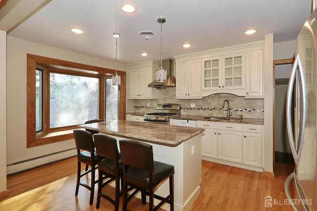 a kitchen with stainless steel appliances granite countertop a stove a sink a microwave oven a refrigerator with white cabinets and wooden floor