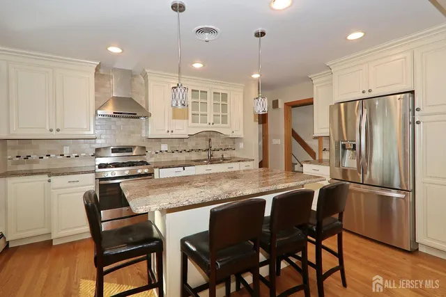 a kitchen with stainless steel appliances granite countertop a sink a stove a refrigerator and island with wooden floor