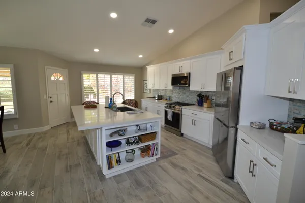 a kitchen with stainless steel appliances granite countertop a refrigerator a stove top oven a sink dishwasher and white cabinets with wooden floor