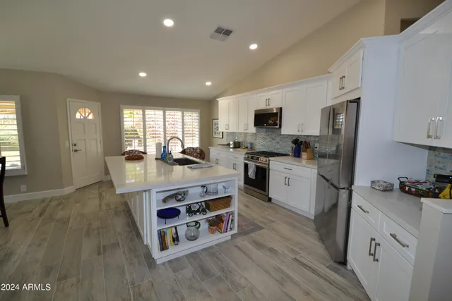 a kitchen with stainless steel appliances granite countertop a refrigerator a stove top oven a sink dishwasher and white cabinets with wooden floor