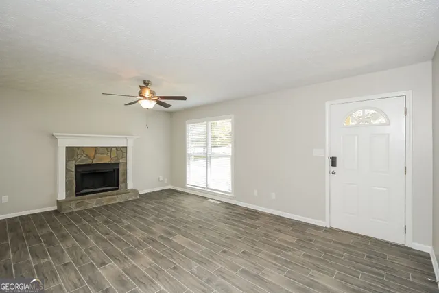 a view of an empty room with wooden floor fireplace and a window