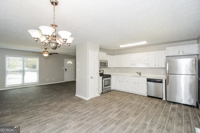 a kitchen with stainless steel appliances granite countertop a refrigerator a sink dishwasher a stove and white cabinets with wooden floor