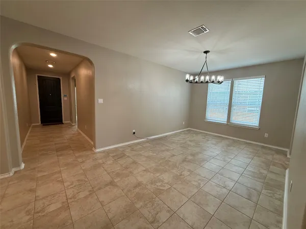 an empty room with kitchen view and chandelier fan