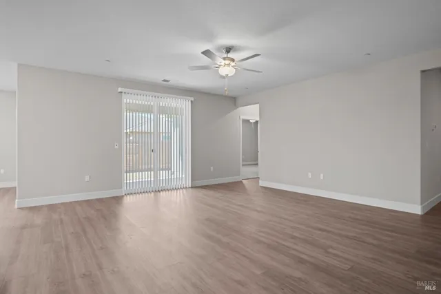 a view of an empty room with wooden floor and a ceiling fan