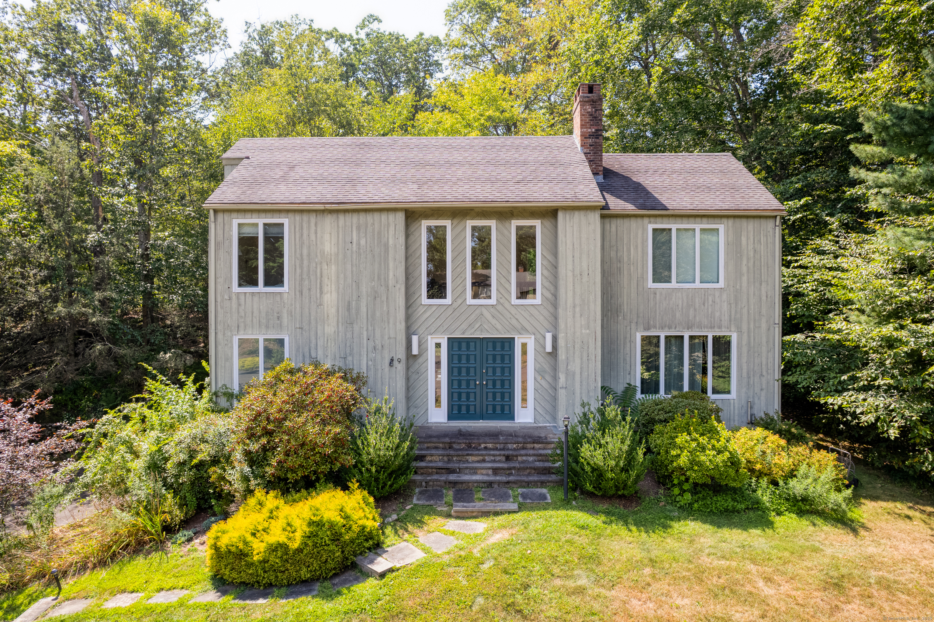 a view of a white house with large windows and a yard with plants and large tree